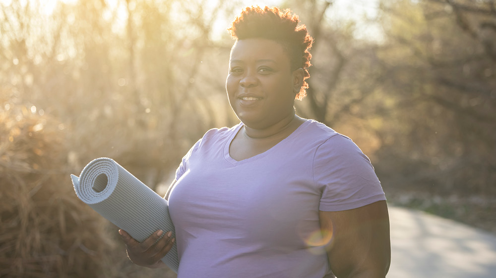Black woman outside in nature with yoga mat