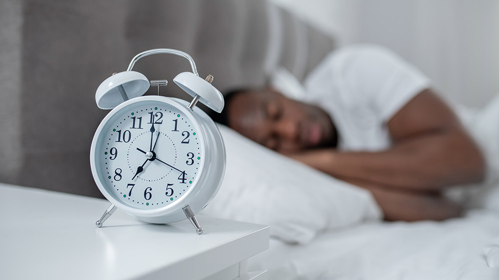 man sleeping in bed with alarm clock on nightstand